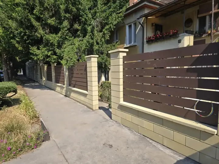 Homokszínű díszzsalukő lábazat és pillérek barna vízszintes WPC léc mezőkkel kertes utcafronton