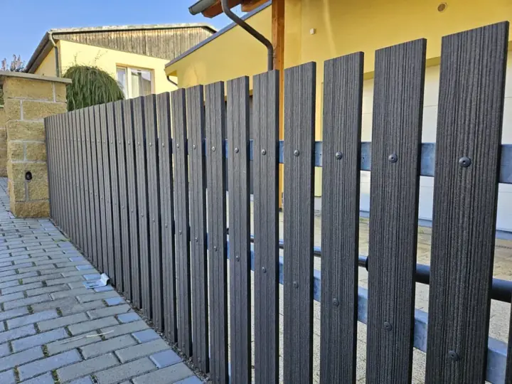 Függőleges, sötét, fa-erezet mintázatú WPC kerítés lécezés közelről, csavaros rögzítéssel
